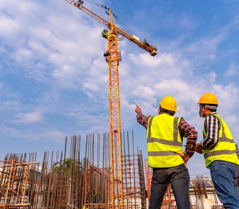 Construction engineers and  architect supervising progress of building construction project stand on new concrete floor top roof and crane background at construction site